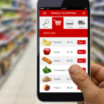 Hand holding a smartphone with a grocery shopping app open in a supermarket aisle.