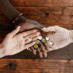 Three people of different skin tones holding bottle caps together on a wooden table, symbolizing unity and connection.